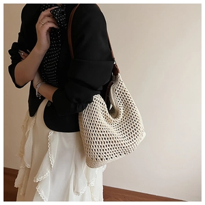 Detail of hand-woven straw tote bag with brown leather strap worn by a model