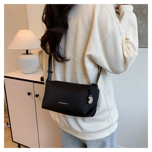 Détail d'un sac bandoulière noir avec pendentif argenté et texte sur un sweat beige