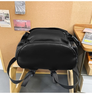 Detail of a black PU leather vintage backpack with multiple pockets on a wooden stool