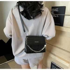 Detail of black crocodile texture handbag featuring decorative pearl and silver metal chain