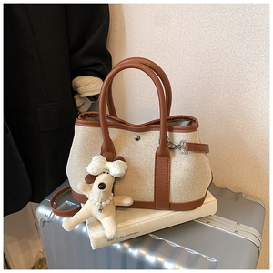 Close-up of cream canvas tote with brown leather trim and cute puppy charm accessory