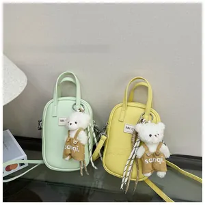 Detail of mini lychee leather crossbody bags in mint and yellow with plush bear charms