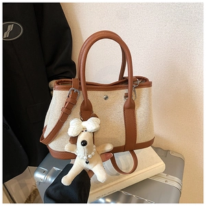 Detail of canvas tote bag with brown leather trim, silver studs and plush dog charm