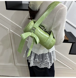 Detail of light green Boston bag featuring a large decorative bow and wide shoulder strap