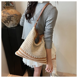 Detail of hand-woven straw tote bag featuring beige stripes and brown leather strap