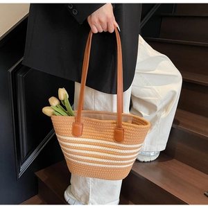 Detail of woven straw tote bag with white stripes and brown leather handle