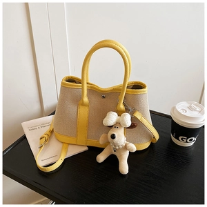Detail of canvas tote bag showing yellow leather trim and cute puppy charm on a table