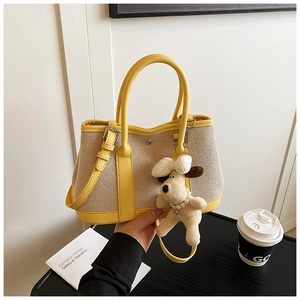 Detail of canvas tote bag in yellow and beige with a plush dog charm and leather handles