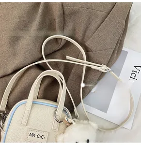 Detail of cream crossbody bag with light blue edges and a plush bear pendant charm