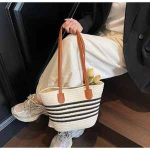 Detail of hand-woven tote bag with black stripes and brown leather handles on stairs