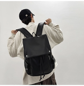 Rear view of model wearing a black matte leather backpack with flap and drawstring closure