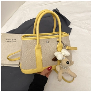 Detail view of canvas tote bag with yellow leather trim and plush puppy pendant accessory
