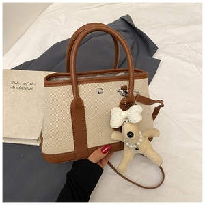 Detail of canvas tote bag with brown leather trim and a cute plush dog pendant charm