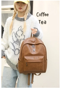 Detail view of brown faux leather backpack with metallic rabbit charm and front zip pocket