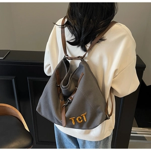 Detail of grey canvas backpack featuring brown leather straps and yellow TCT embroidery