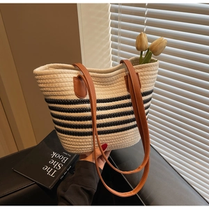 Detail of woven straw tote bag featuring navy stripes and brown leather handles