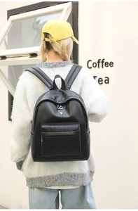 Detail of black leather backpack with silver deer head logo and metal ring zippers