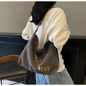 Detail of grey canvas tote bag featuring brown leather straps and yellow TCT lettering