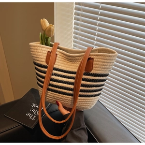 Detail of woven rope tote with navy stripes and brown leather handle on a sofa