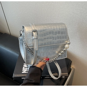Detail of silver crocodile-patterned square bag with metallic chain and pearl strap