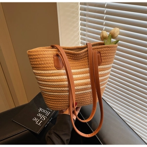 Close-up of woven straw tote bag featuring brown leather straps and striped rope texture