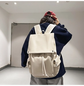 Rear view of a person wearing a beige faux leather flap backpack in a minimalist room