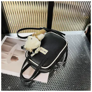 Detail of black lychee grain leather handbag with white piping and plush rabbit charm