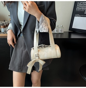 Détail du sac Boston crème avec un grand nœud et une large bandoulière sur un mannequin