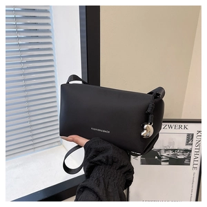 Détail du sac à bandoulière en cuir noir mat avec texte mode blanc et breloque coeur