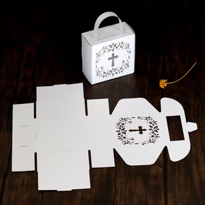 Flat lay of laser-cut white cross favor box with assembly guide on dark wood background