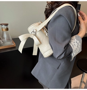 Détail du sac cylindre blanc crème avec grand nœud 3D et texture en similicuir mat