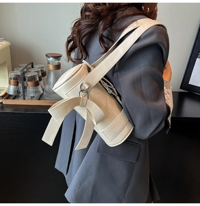 Detail of cream-white cylinder bag featuring large side bow and wide shoulder strap