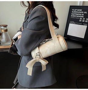 Detail of cream Boston bag with leather texture, bow pendant and wide shoulder strap