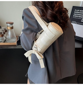 Détail du sac cylindrique beige avec nœud surdimensionné et texture en similicuir lisse