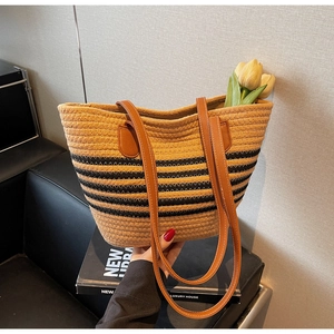 Close-up of woven straw tote bag with black stripes and premium brown leather handles