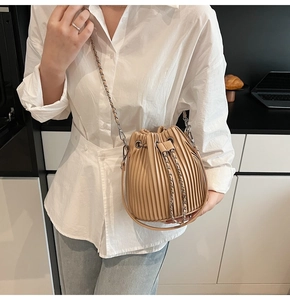 Close-up of pleated beige bucket bag with silver chain strap worn by a model