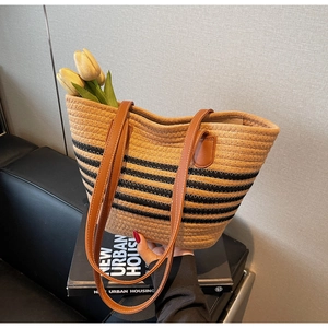 Detail of woven tote bag with black stripes and brown leather shoulder straps