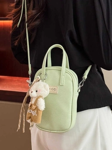 Light green pebble grain crossbody bag with cute plush bear charm on a female model