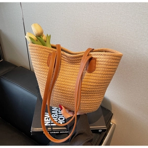Detailed texture of hand-woven straw tote bag with brown leather shoulder straps