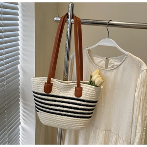 Detail of woven beach tote with black stripes and brown leather straps on a clothes hanger