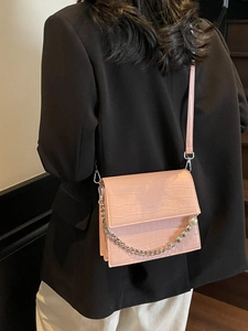 Pink croc-embossed crossbody bag with pearl chain and fashion logo on black blazer