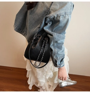 Detail of pleated black bucket bag featuring metal chain strap on model for shoulder wear