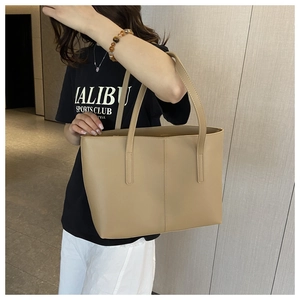 Minimalist beige leather tote bag with long handles styled on a model in a modern hallway