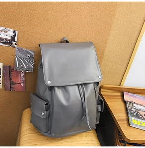 Detail of minimalist gray backpack on wooden chair with drawstring and flap closure