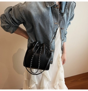 Detail view of black pleated bucket bag with silver metal chain and drawstring closure