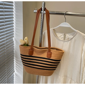 Close-up of woven tote bag with black stripes and brown leather strap with white stitching