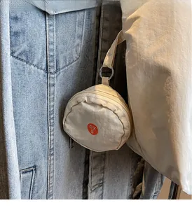 Detail of a beige round mini clip-on nylon pouch with zipper and metallic D-ring hook