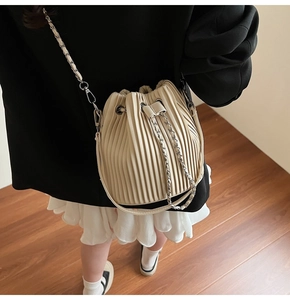 Detail of off-white pleated bucket bag featuring metal chain strap and drawstring closure