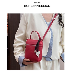 Détail d'un sac à main rouge en cuir grainé avec pendentif coeur sur un blazer blanc