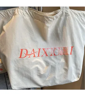 Detail of soft cream canvas tote bag featuring red DAIXISHI logo and textile texture